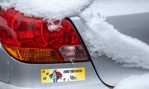 Back bumpers of snow covered white sedan. There is a bumper sticker of an evil robot Santa. Text reads Ho Ho Ho and Choose Your Fighter.