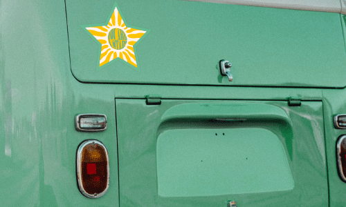 Back bumper of teal van. Die-cut star shaped sticker in geometric patter of yellow and white.