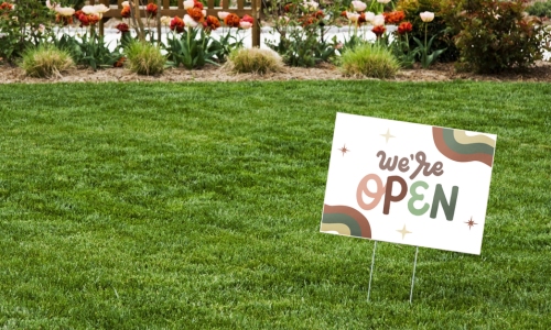 Yard sign in lawn that says "we are open"