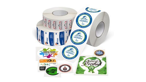The roll of labels with circle labels in blue and green, and rectangle labels in red white and blue. Circle label in CMYK colors, rounded corner label in orange white and black, and three smaller individual circle labels with colored lettered logos.